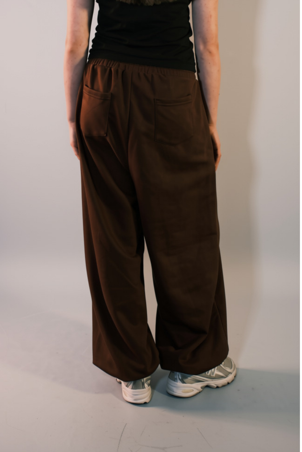 A person shown from the back wearing loose, wide-leg brown pants with an elastic waistband and side pockets, paired with a black top.
